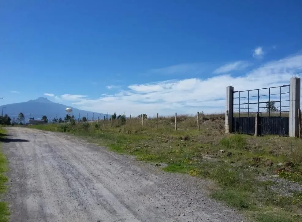 Portón metálico entre dos columnas de concreto sobre el camino de acceso al polígono.
