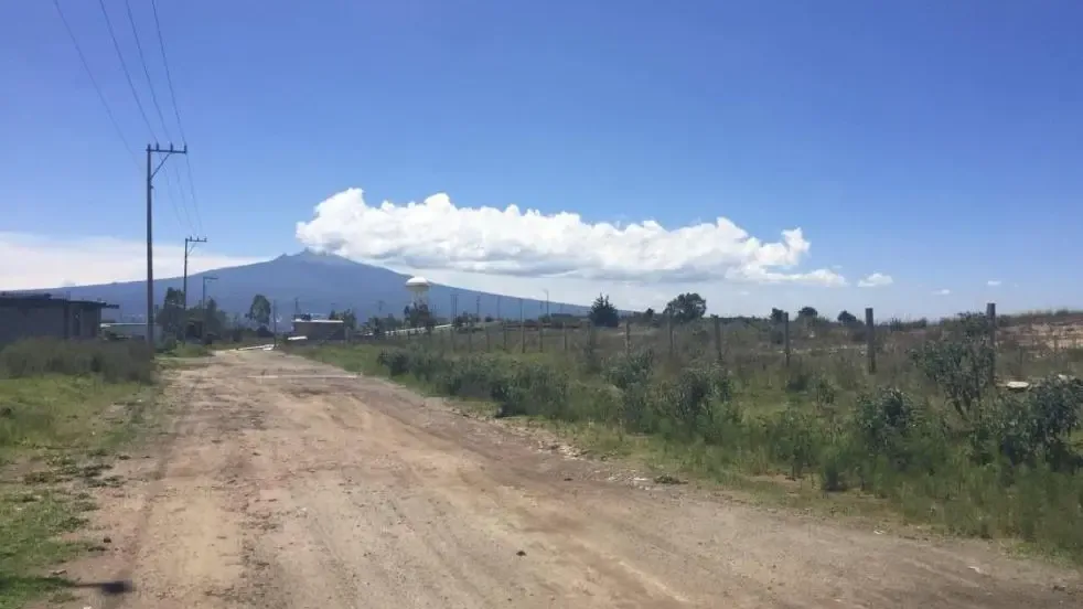 Camino de terracería que bordea el predio, con postes de luz y La Malinche al fondo.